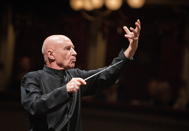Intense moment of Christoph Eschenbach conducting, raising his left arm while holding the baton in his right. Photography.