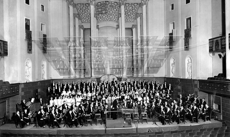 Black and white photo of the conductor and the orchestra posing in the main hall of Konserthuset.