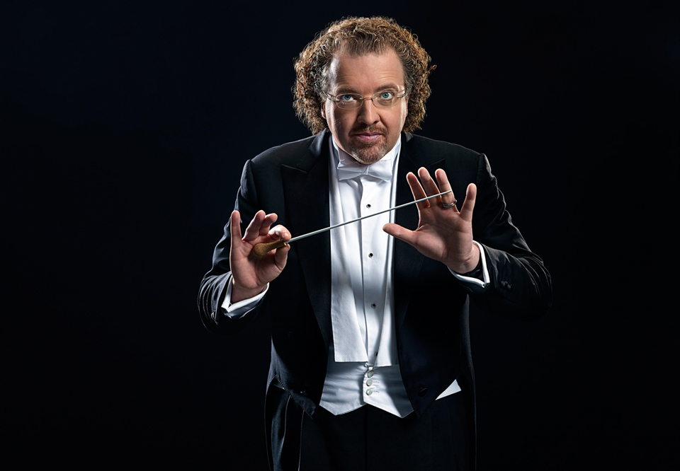 Conductor Stéphane Dénève in a photo studio environment, looking straight at the camera and making a conductor's pose with his hands. Photography.
