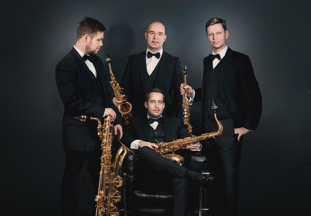 Gruppbild på kvartetten. Tre stycken uppklädda män står runt ytterligare en som sitter ner. Alla håller i var sin saxofon. Fotografi.