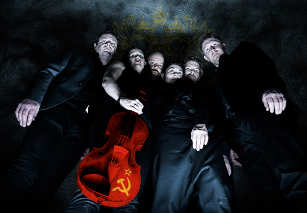The standing standing, one members holds a violin painted in red with the hammer and the sickle in yellow. Photography.