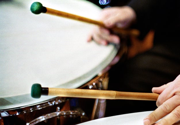 Close up of timpanist playing, showing hands holding the sticks above the timpani. Photography.