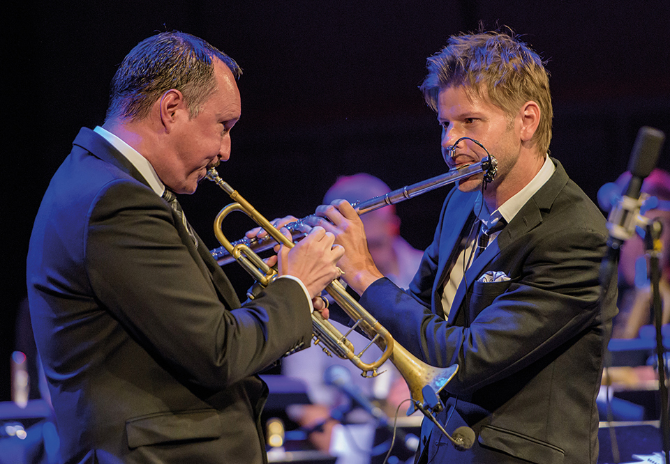 Peter Asplund and Magnus Lindgren standing close and looking straight at each other whle playing during a live concert. Photography.