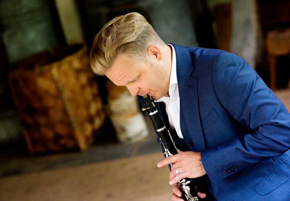 Christoffer spelar på sin klarinett i profil. Finklädd. Fotografi.