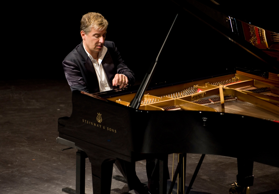 Pianist Jean-Yves Thibaudet sitting at the piano playing in the upper register of the keyboard with great concentration. Photography.