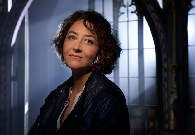Close-up of the singer Nathalie Stutzmann, looking in to the camera in a dimly lit church environment. Photography.