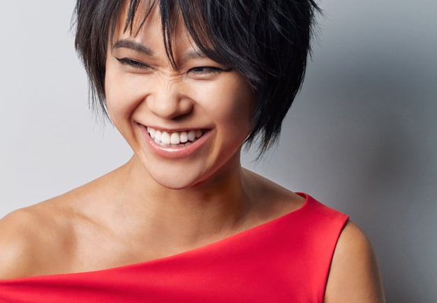 Close-up of the pianist Yuja Wang dressed in red, smiling and slightly frowning her nose. Photography.