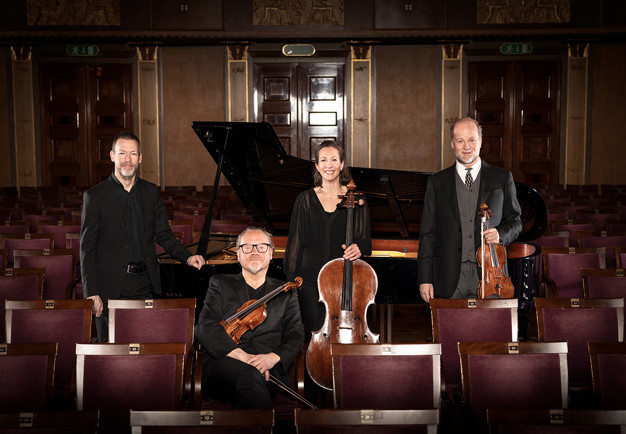 Fyra musiker som sitter och står blands stolarna i Grünewaldsalen. Fotografi.