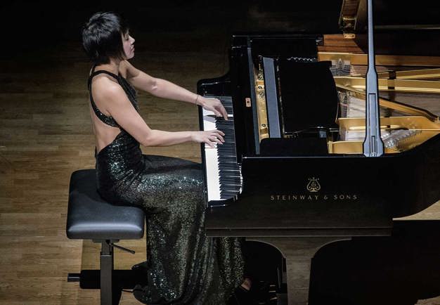 Woman in black long dress energetically plays on a grand piano. Concert Photography.