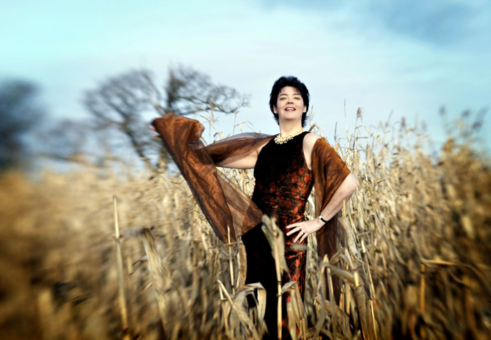 Kvinna i ett vetefält med brun klänning. Fotografi.