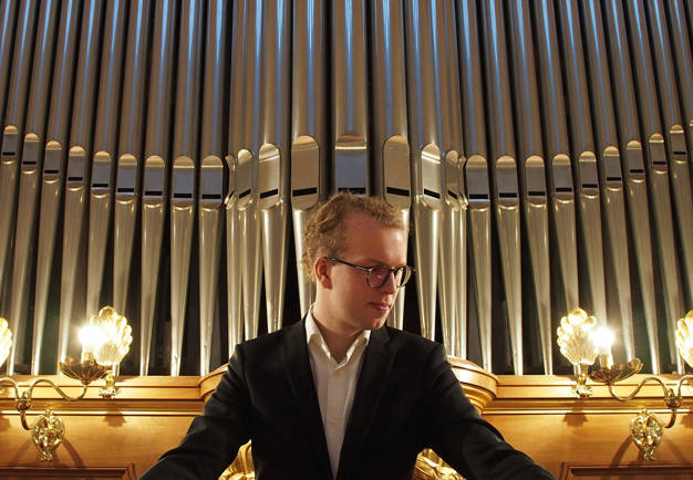 Man standing in front of an organ. Photo.