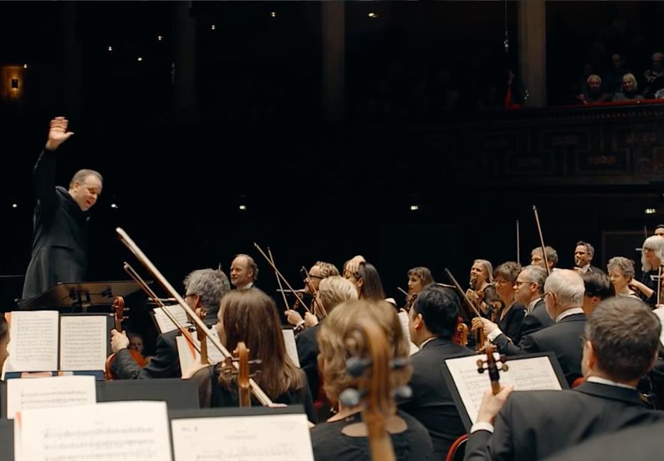 Man dirigerar med kraft, konsertklädda musiker i orkestern. Fotografi