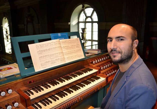Man in blue jacket sitting at an organ. Looking into the camera.