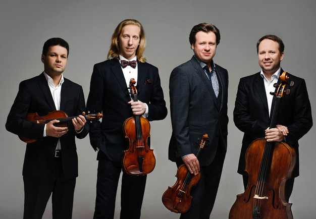 Fyra män på rad. Alla håller sina instrument i famnen. Foto