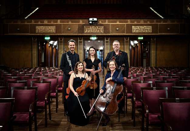 Photography of the ensemble holding their instruments. Dark background