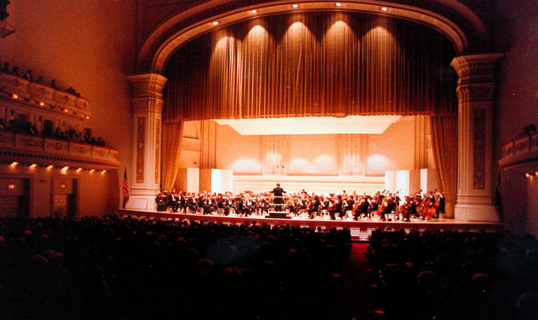 Upplyst scen sedd på avstånd från publikplats. Gruppfotografi av Yuri Ahronovitch och orkestern i Carnegie Hall den 31 oktober 1984.