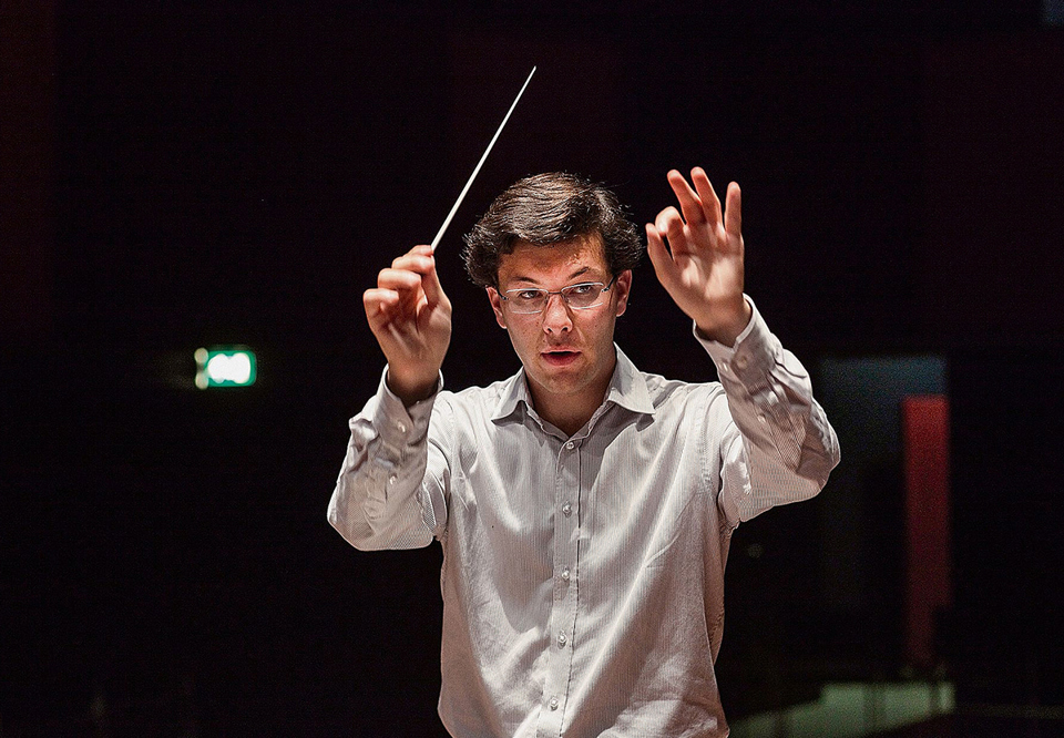 Man with white shirt conducting. Photo.