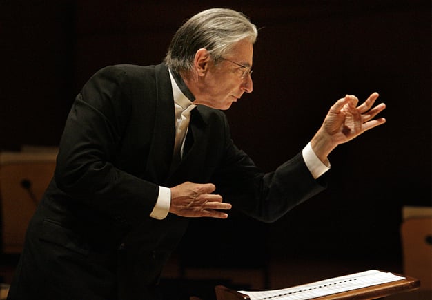 Conductor Michael Tilson Thomas in concert, focused and with his left hand making a pointillistic sign. Photography.