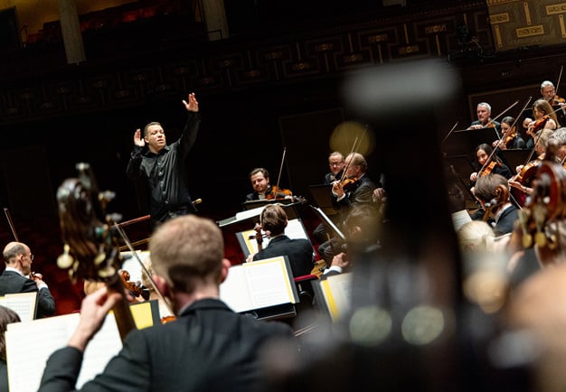 symfoniorkester som spelar och leds av dirigent. Fotografi