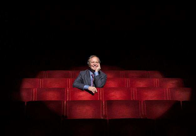 Man seated in one of the red chairs in the stalls. Photography.