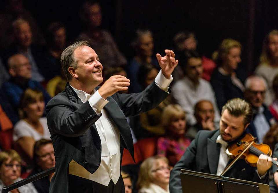 Man conducting large orchestra. Photo.