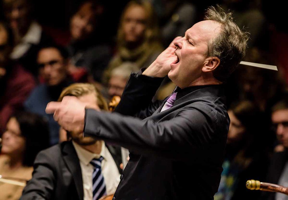 Man som dirigerar stor symfoniorkester. Fotografi.