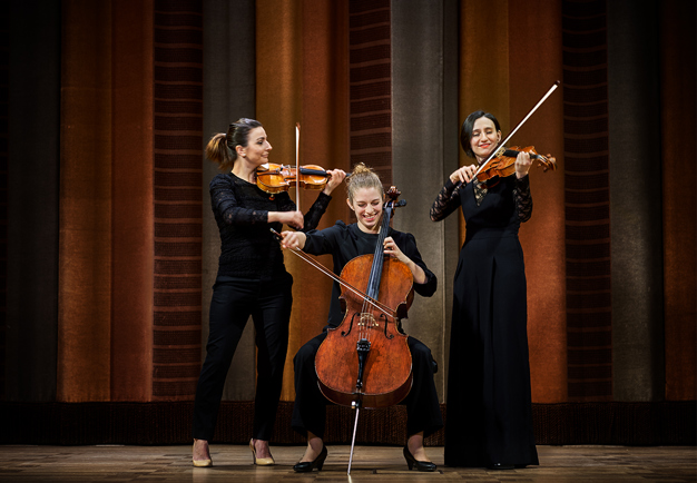 Tre kvinnor som står på scen. Två spelar fiol och en spelar cello.