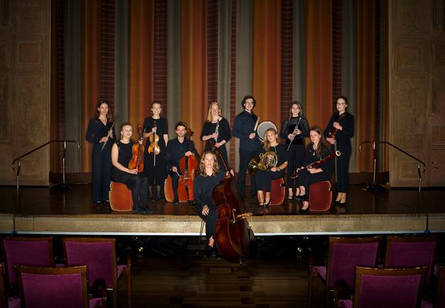 Samling av unga musiker som står på en scen med sina instrument. Fotografi.