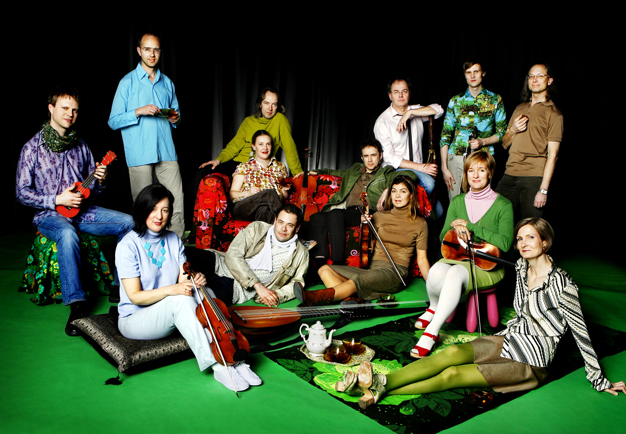 A very colourfully dressed ensemble sitting and standing on a bright green carpet. Photography.