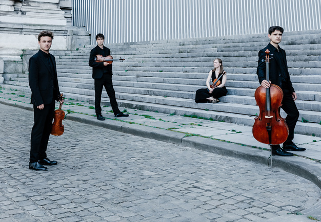 Fyra musiker som ståre och sitter. Fotografi.