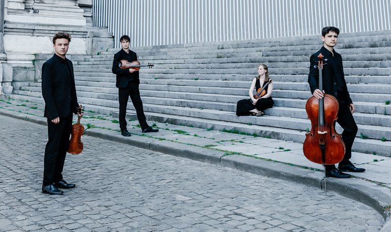 Fyra musiker som står och sitter. Fotografi.