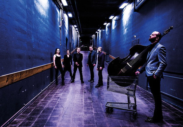 Five muscians in a blue corridor with the instruemnt in their hands. Photography.