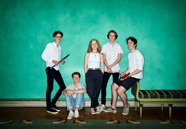 Fem ungdomar som lutar sig mot en grön vägg. Fotografi