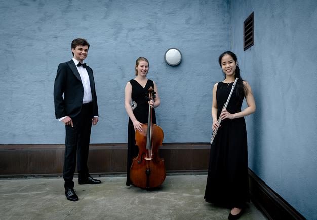 Tre musiker som står med sina instrument mot en bklå vägg. Fotografi.