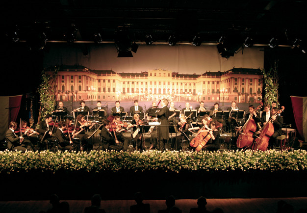 Hela orkestern med dirirgent framför sig.Schönbrunn Slottsfilharmoniker. Fotografi.