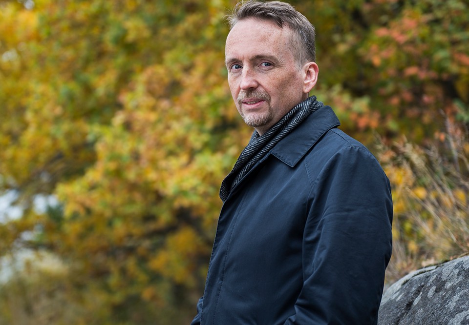 Man som tittar in i kameran med skog bakom sig. Foto.