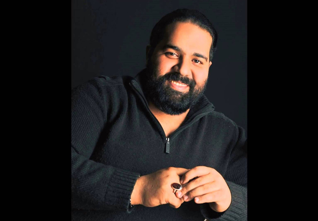 Reza Sadeghi sitting and smiling to the camera. Photography.