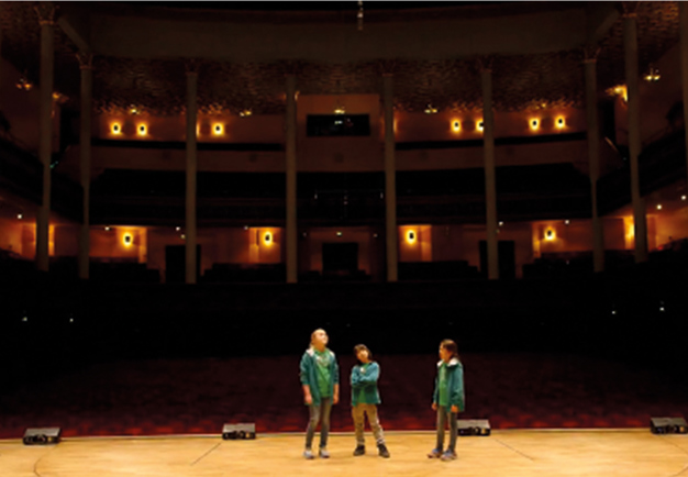 Utdrag ur filmen. Tre barn på podiet i Konserthusets stora sal. Fotografi.