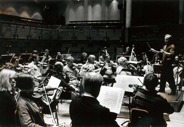 Black and white photograph from a rehearsal in the main hall, the conductor is viewed from the side as well as large parts of the musicians.
