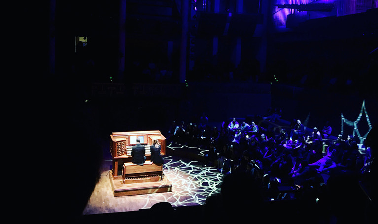 Organ on stage in a dark room, with a spot light on it. Photo.