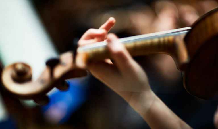  Hand holding fingers on the strings of a violin. Photo.