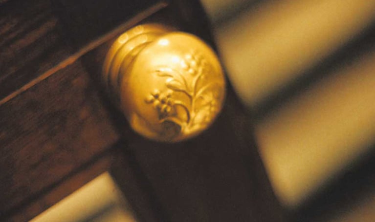 Detaljbild på en dörrknopp, guldig och vackert utsmyckad. Fotografi.