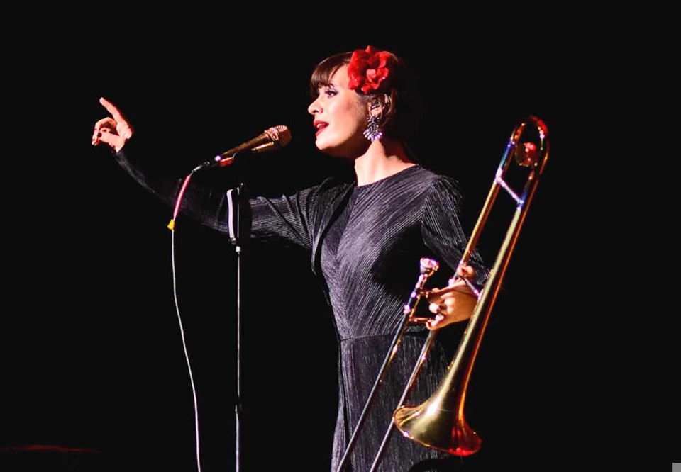 Aubrey står med sin trombon på scenen. Konsertsituation. Fotografi.