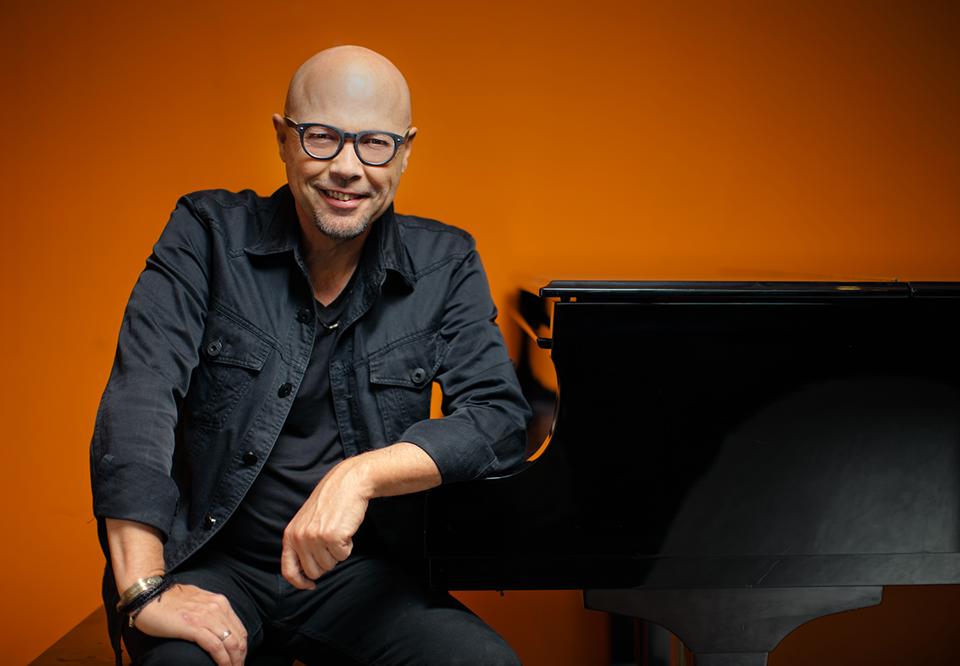 John Beasley sitting by his piano. Photo.