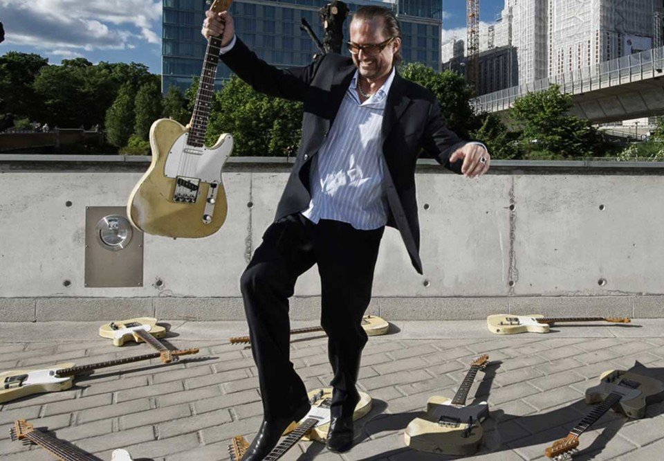 Max Schultz står mitt bland ett hav av gitarrer som ligger utslängda. Fotografi