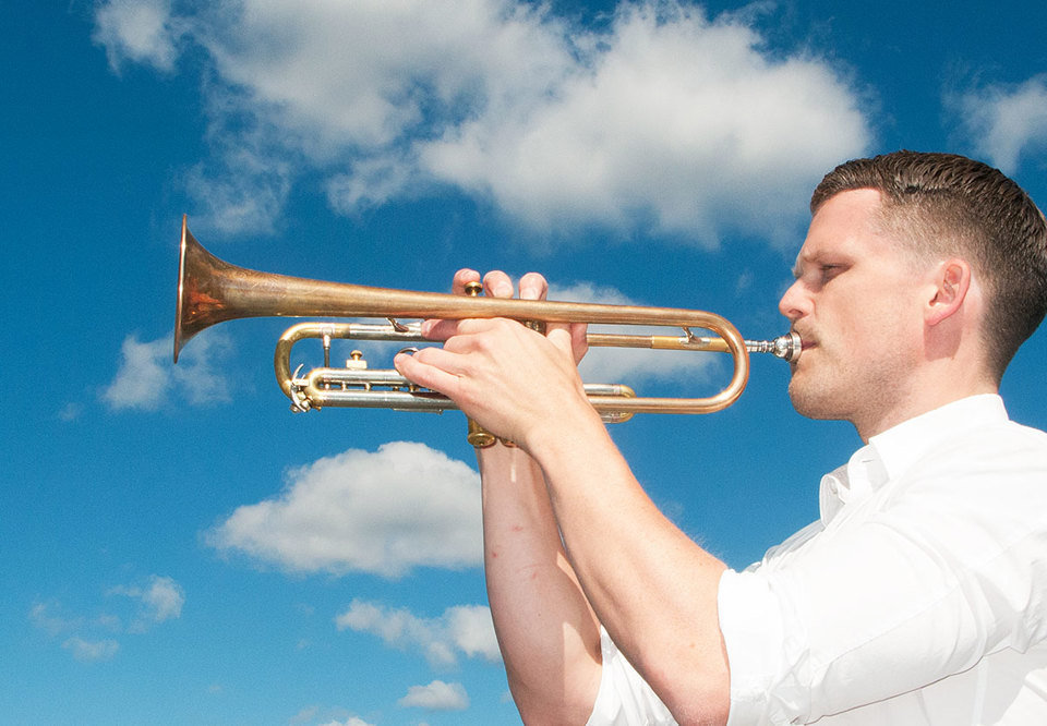 Man som blåser trumpet ute. Klarblå himmel i bakgrunden.