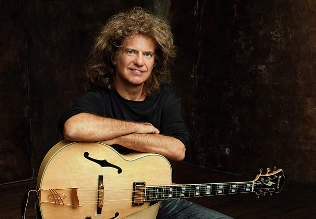 Guitarist Pat Metheny looking into the camera sitting on a chair, in a black t-shirt and with the guitar in his lap. Photography. 