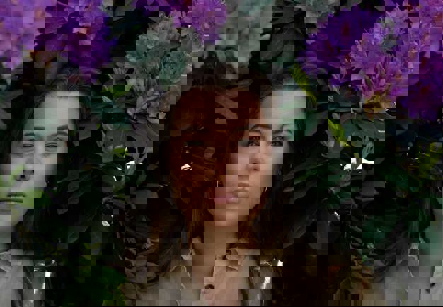 Woman standing among purple flowers. Looking into the camera. Photography.