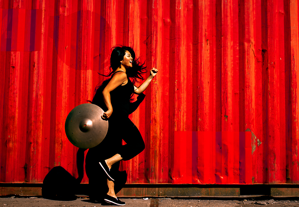 Kvinna som springer framför röd vägg med cybal. Fotogrfi.
