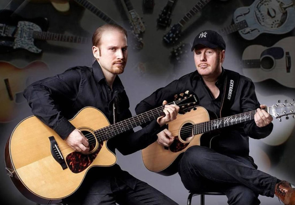 Två män med gitarrer i knät. Fotografi.